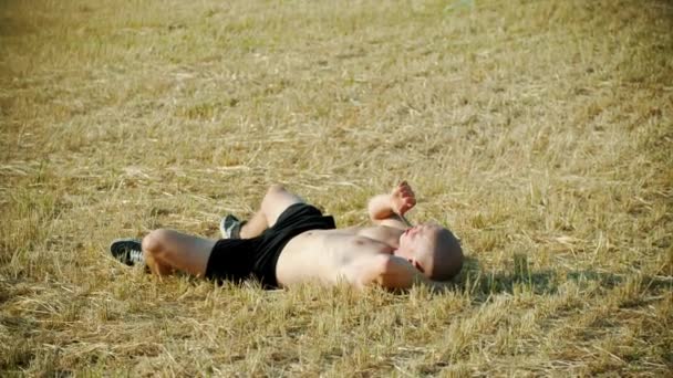 Plešatý muž ležící na poli a kouřící cigaretu - pozorující oblohu — Stock video