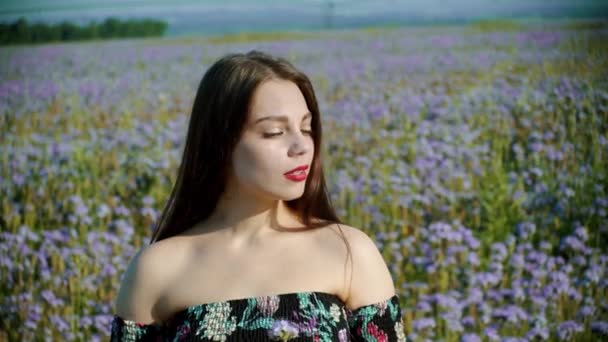 Romantic young woman standing on the flower field and holding a blue flower in front of the sun — Stock Video