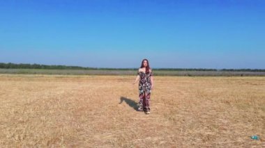 Sarı tarlada yürüyen gevşek elbiseli romantik genç kadın.