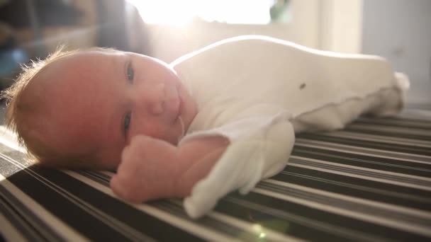 Ένα μικρό χαρούμενο νεογέννητο μωρό ξαπλωμένο στην πλάτη του σε ριγέ επιφάνεια και κοιτάζοντας στην κάμερα — Αρχείο Βίντεο