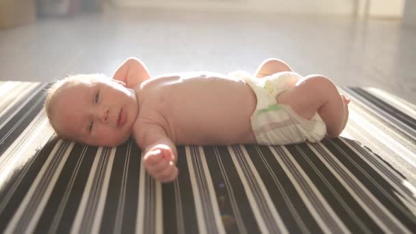 Ein kleines Baby in einer Windel liegt auf dem Rücken auf einem gestreiften Laken und bewegt seine Beine und Hände — Stockvideo