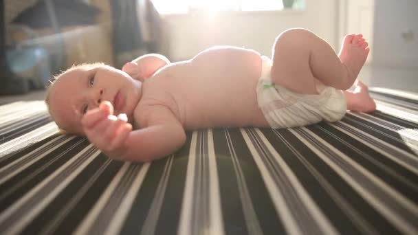Un petit bébé dans une couche couché sur le dos sur des draps et bougeant ses jambes et ses mains — Video