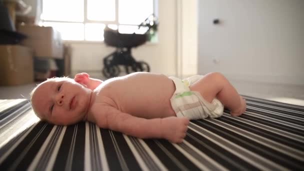 Un pequeño bebé con un pañal acostado boca arriba sobre sábanas a la luz del día y moviendo las piernas y las manos — Vídeo de stock