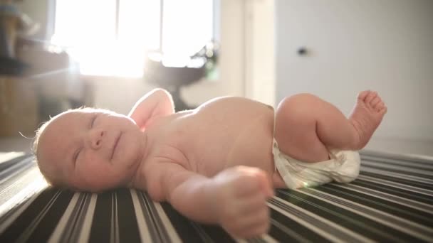 A little happy baby in a diaper lying on his back on sheets in day light and moving his legs and hands — Stock Video