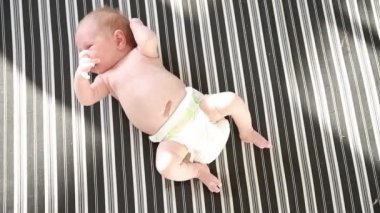 Beyaz bezli şirin, aktif bir bebek çizgili çarşafların üzerinde yatıp hareket ediyor.