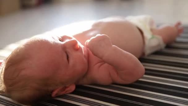 Un petit bébé dans une couche couché sur le dos sur des draps rayés à la lumière du jour — Video