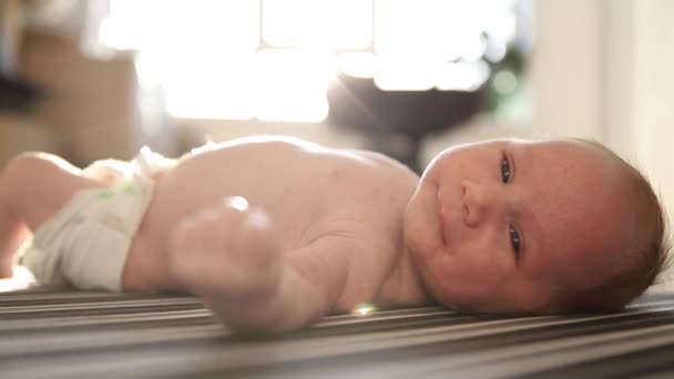 Un petit bébé dans une couche couché sur le dos sur des draps rayés à la lumière du jour — Video