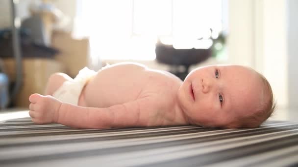 Un petit bébé mignon dans une couche couchée sur le dos sur des draps rayés — Video