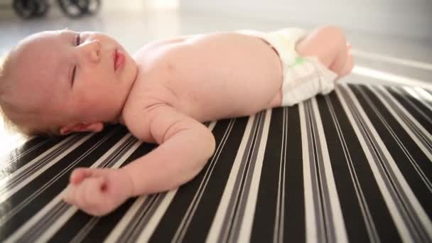 Un bébé nouveau-né mignon dans une couche couchée sur le dos sur des draps monochromes rayés — Video