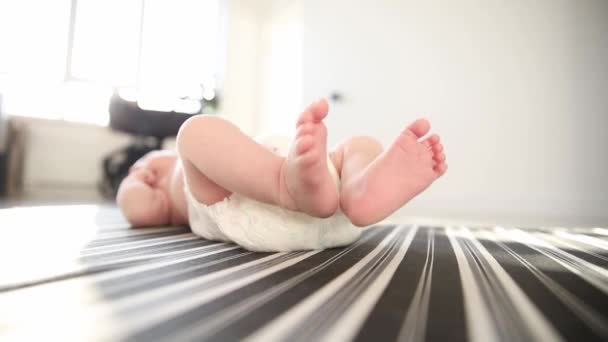 Un bebé recién nacido con un pañal blanco acostado en la cama y moviendo las piernas — Vídeo de stock