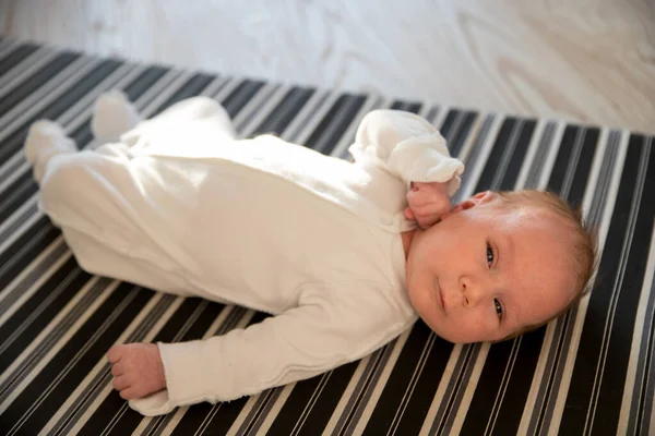 Een kleine schattige pasgeboren baby liggend op zijn rug op gestreept laken — Stockfoto