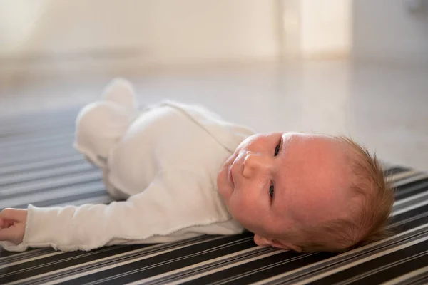 En liten söt nyfödd bebis som ligger på rygg på randig monokrom lakan — Stockfoto