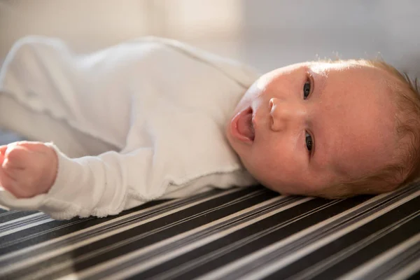 Ett litet nyfött barn med öppnad mun på ryggen på randig monokrom lakan — Stockfoto