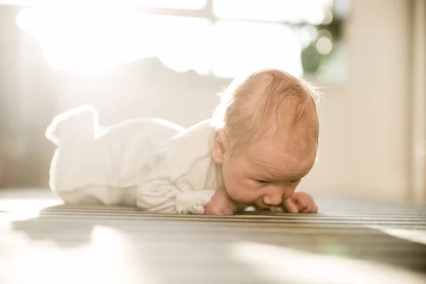 Ett litet nyfött barn som ligger på magen på randigt lakan och tittar ner. — Stockfoto