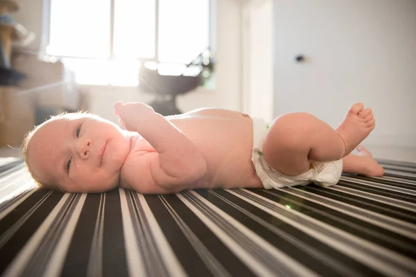 Um bebê recém-nascido em uma fralda deitado em uma cama inventada — Fotografia de Stock