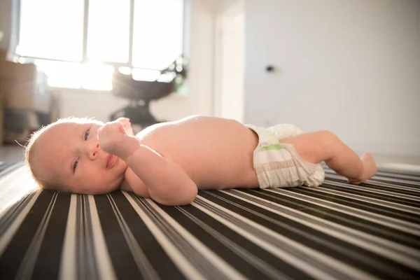 Um bebê recém-nascido em uma fralda deitado em uma cama listrada — Fotografia de Stock