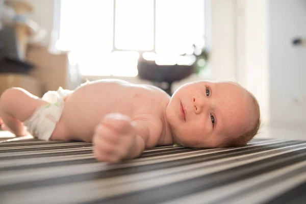 Um pequeno bebê bonito em uma fralda inquieto deitado de costas em lençóis listrados — Fotografia de Stock