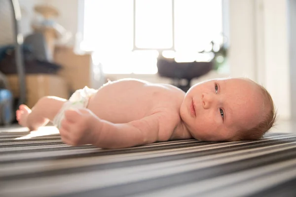 薄日の光の中で縞模様のシートの上に彼の背中に横たわっオムツの新生児 — ストック写真