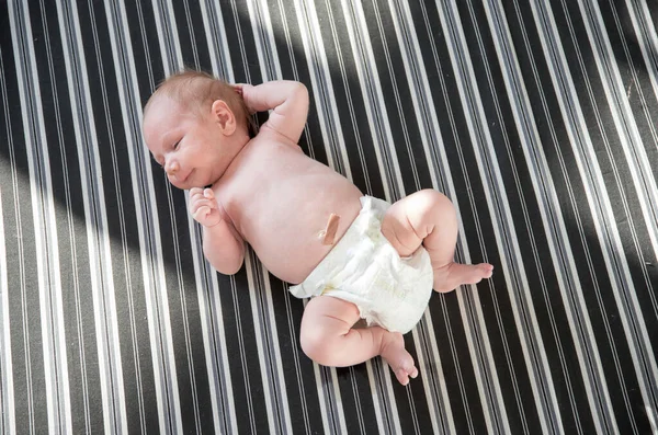穿着白色尿布躺在条纹床单上的可爱新生儿 — 图库照片