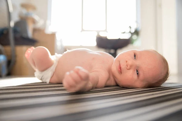一个穿着尿布的新生婴儿不安分地躺在带条纹的床单上 — 图库照片