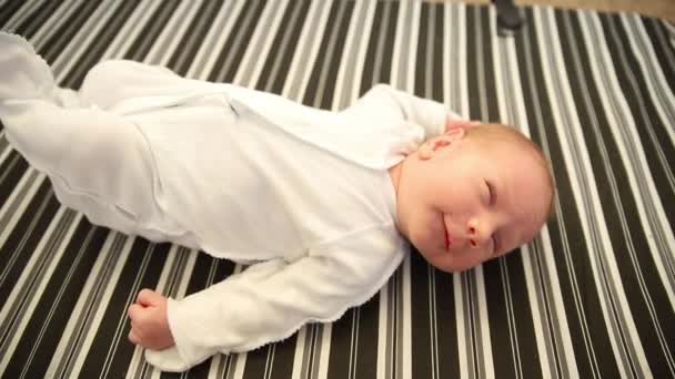 Un nouveau-né en costume blanc couché sur le dos sur un drap rayé - parent jouant avec sa petite main — Video
