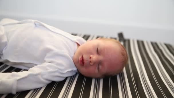 Un nouveau-né en costume blanc couché sur le dos et actif — Video