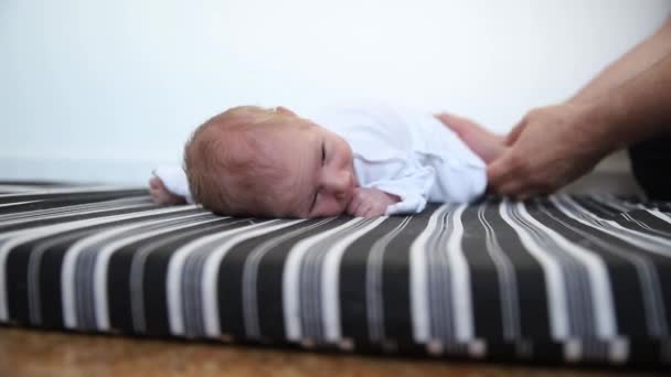 Een pasgeboren baby in wit kostuum liggend op zijn buik en zijn ouders houden hem van achteren vast — Stockvideo