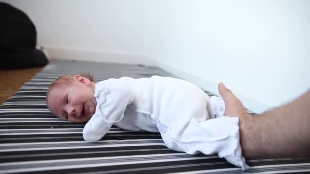 Egy újszülött fehér jelmezben fekszik a hasán, és a szülei nyomják a lábait. — Stock videók