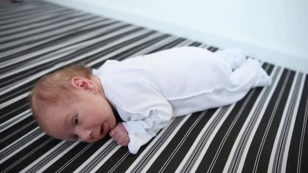 Egy újszülött fehér jelmezben fekszik a hasán és mozog. — Stock videók