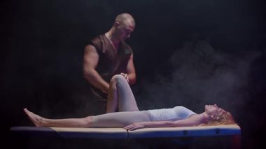 Bir kayropraktik uzmanıyla seans. Sırtüstü uzanmış genç bir kadın. Terapist bacağını eğip karnına bastırıyor.