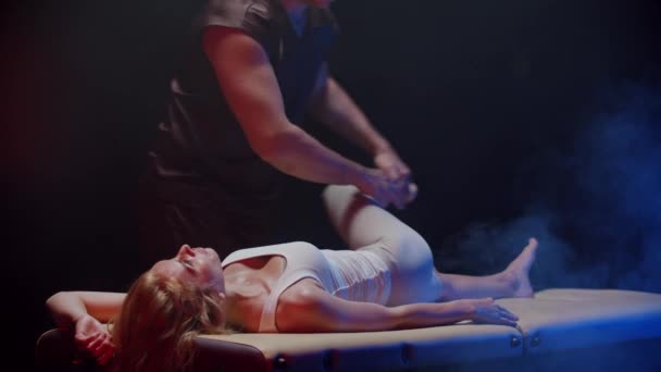 Bir kayropraktik uzmanıyla seans - terapist kadın müşterisinin bacağını kenara çeker ve üzerine bastırır. — Stok video