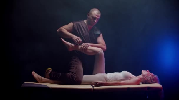Sesión con un masaje - mujer joven acostada boca arriba y el quiropráctico terapeuta dobla la pierna y la mueve hacia su cuerpo — Vídeo de stock