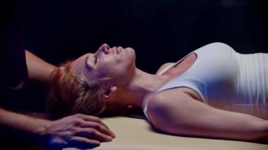 Karanlık stüdyoda kayropraktik terapi. Kadın müşterisinin boynuyla çalışan bir erkek terapist.