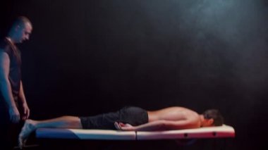 Karanlık stüdyoda kiropraktik terapi. Bir terapist müvekkilini kanepeye oturtuyor.