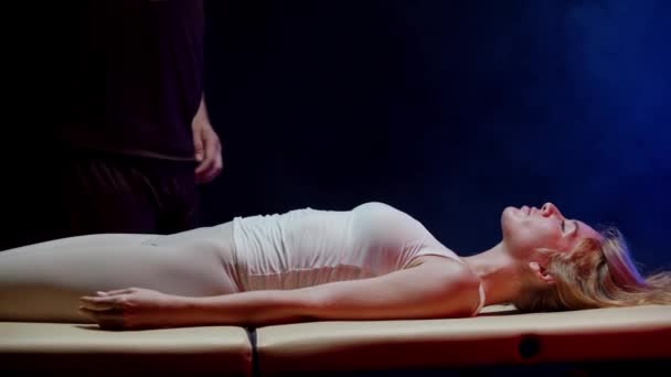 Молодая женщина проводит сеанс хиропрактики в темной студии - терапевт, работающий с ее телом — стоковое видео