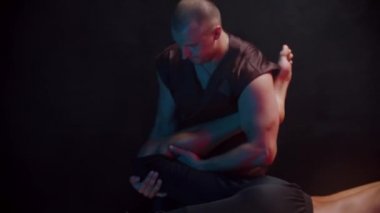 Stüdyoda kiropraktik terapi görüyor. Bir terapist, hastasının bacağını karnının üstünde yatarken hareket ettiriyor.