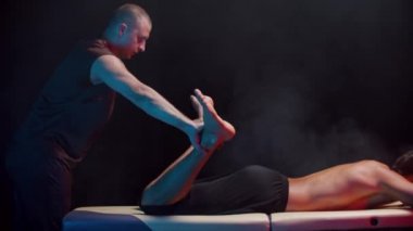 Smoky stüdyosunda kiropraktik terapi. Bir terapist, müşterisinin bacaklarını birbirinden ayırır.