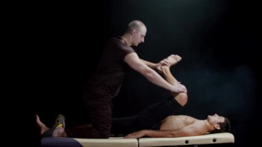 Karanlık stüdyoda kiropraktik terapi. Müvekkilinin bacaklarıyla çalışan bir terapist.