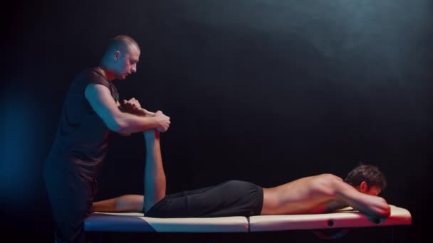 Chiropraktická terapie v temném ateliéru - terapeut masírující nohu svého klienta — Stock video