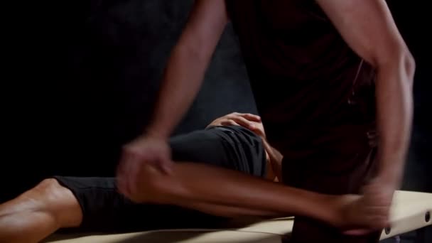 Smoky stüdyosunda kiropraktik seansı. Müvekkilinin bacaklarıyla çalışan bir terapist. Kalça eklemini oynatıyor. — Stok video