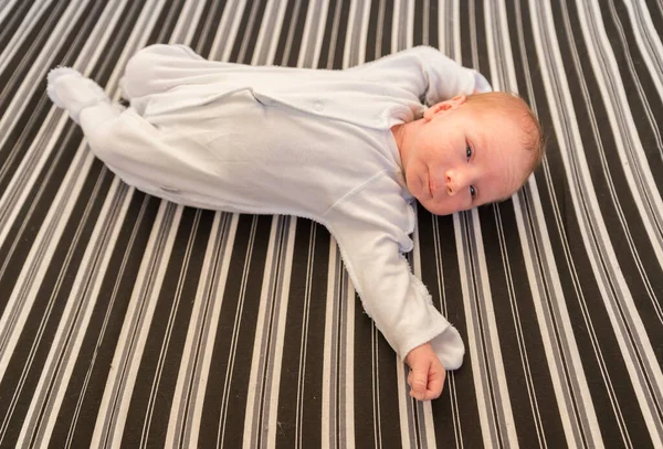 Baby liggande på rygg på randigt lakan — Stockfoto