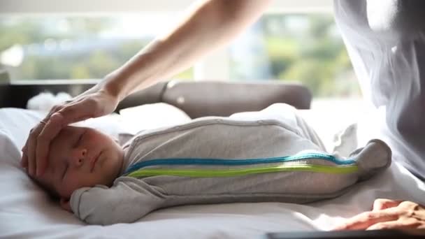 Ginger woman mother gently patting her little baby lying on the baby cot — Stock Video