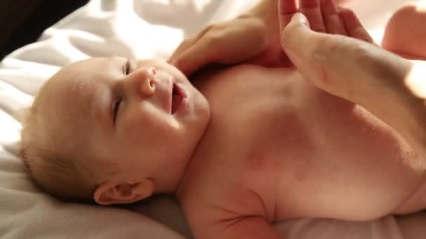 Nyfødt smilende baby liggende på sengen på ryggen og hans forældre masserer ham – Stock-video