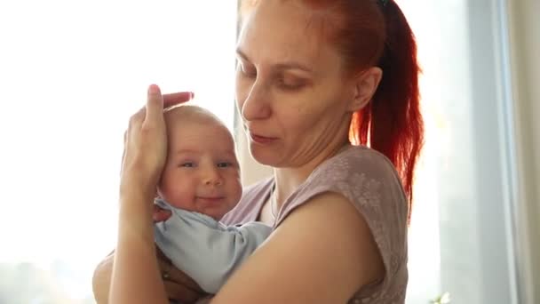 Mulher de gengibre segurando seu bebê pequeno e batendo-lhe de pé pela janela — Vídeo de Stock