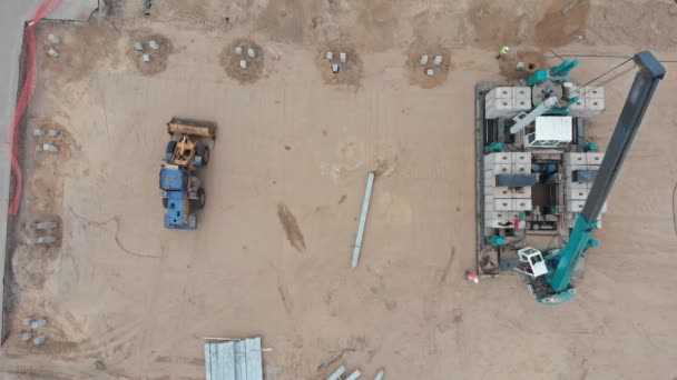 Hebekran auf der Baustelle hebt längliche Betonklötze und herumlaufende Menschen auf dem Gelände — Stockvideo