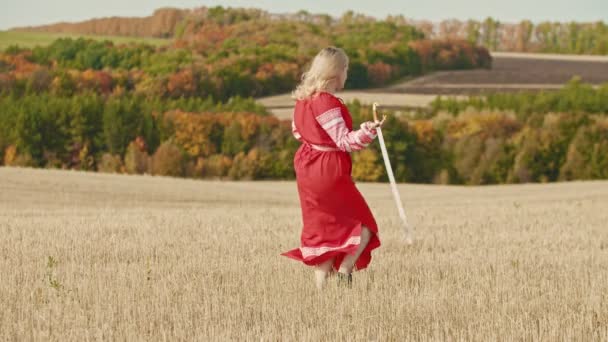 Young beautiful woman in long dress standing on the field and playing with a sword then drops it — Stock Video