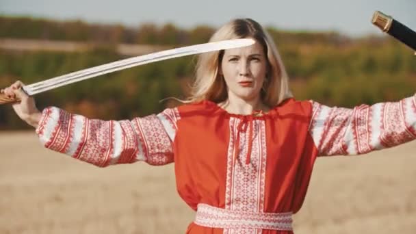 Junge Frau in Kleid steht auf dem Feld und zieht ein Schwert aus der Scheide — Stockvideo