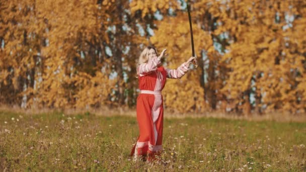 Vrouw in rode nationale jurk op het veld en schermen met een zwaard — Stockvideo