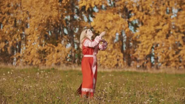 Vrouw in rode nationale jurk staan op het veld en schermen met een zwaard - gooit het op en vangen het — Stockvideo