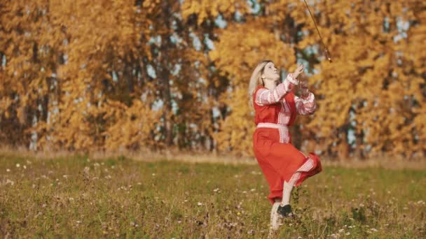 Sterke vrouw in rode nationale jurk staat op het veld en schermen met een zwaard — Stockvideo